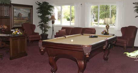 A cozy living room featuring a billiard table, sofas, and large windows.