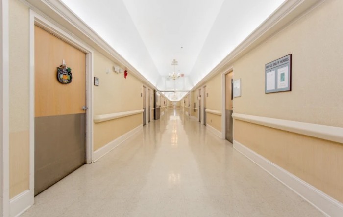 A brightly lit hospital corridor with beige walls and multiple doors on either side.