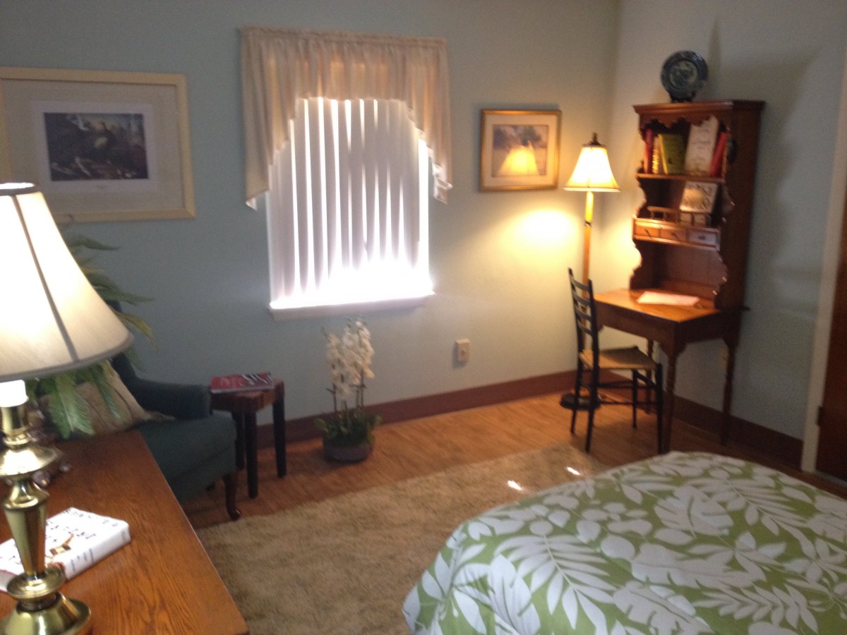 A cozy and well-lit bedroom featuring a wooden desk, chair, and a lamp near a window with curtains.