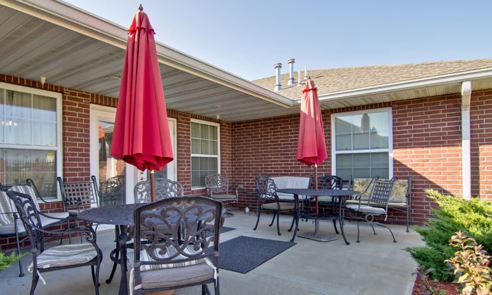 A cozy patio area with red umbrellas and metal furniture against a brick building backdrop.