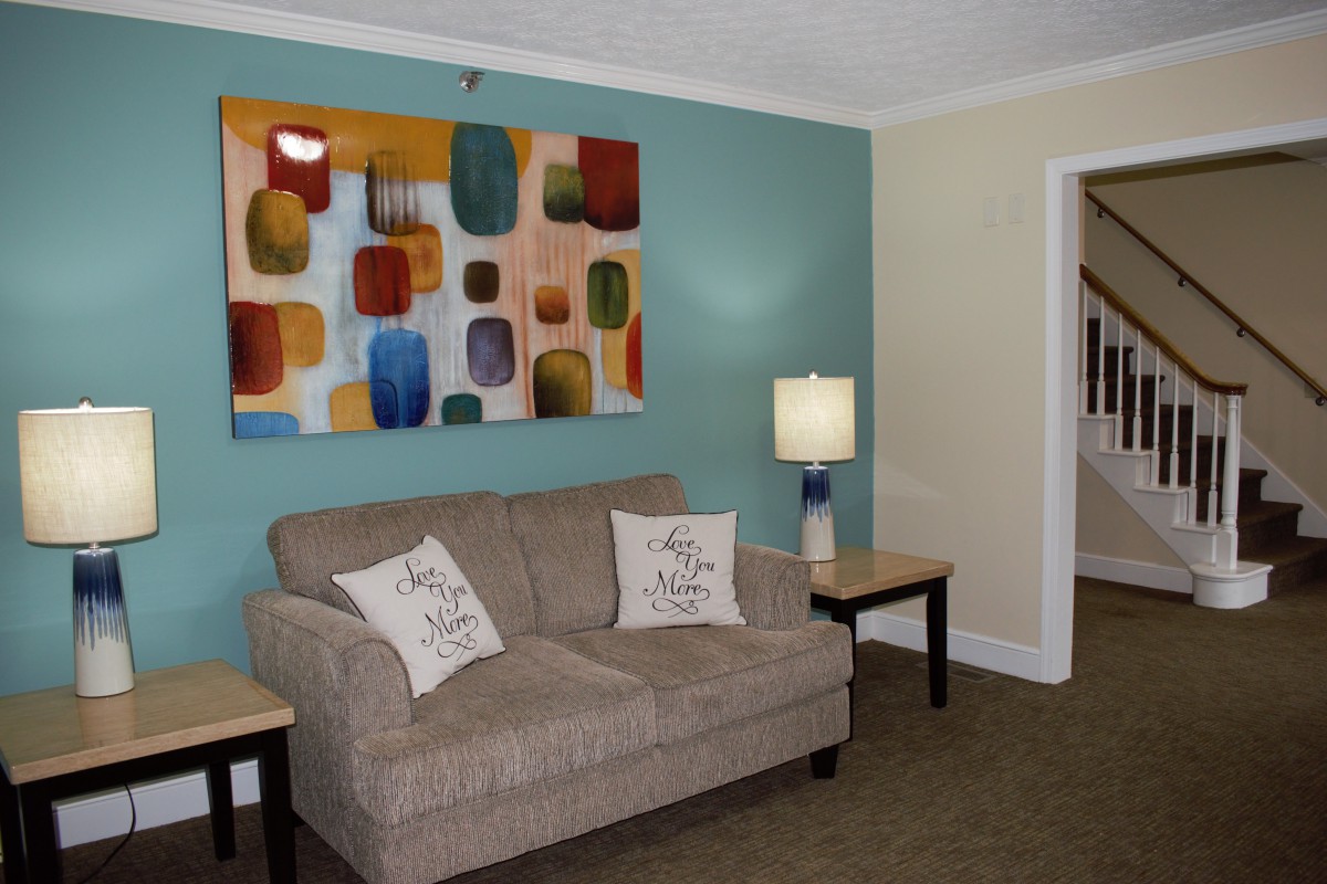 A cozy living room with a beige sofa, colorful abstract wall art, and a lamp on a side table.