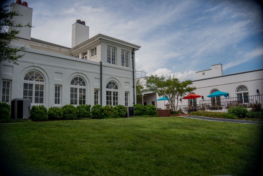 A scenic view of a white building with arched windows and a well-maintained lawn under a cloudy sky.