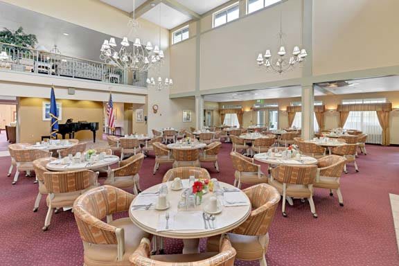 A spacious dining room with elegant chandeliers, round tables, and plush chairs.
