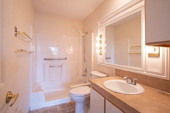A bright bathroom with a shower, toilet, and sink beneath a large mirror.