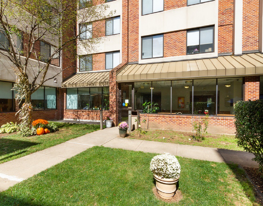 An exterior view of an apartment building with a well-maintained lawn and flower arrangements near the entrance.