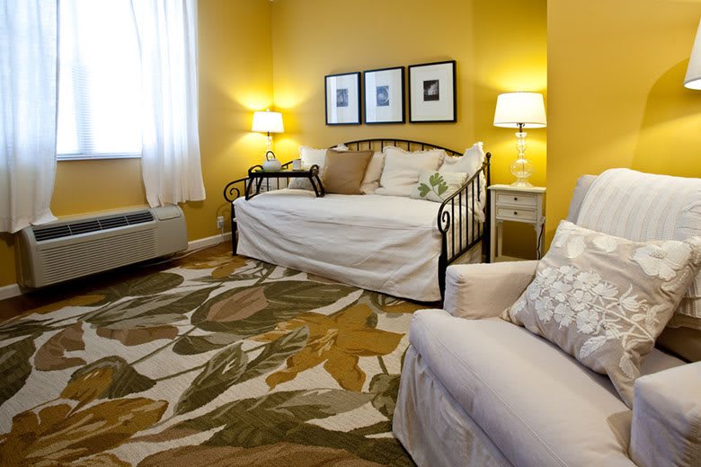 A cozy living room with yellow walls, featuring a daybed, patterned rug, and soft lighting from lamps.