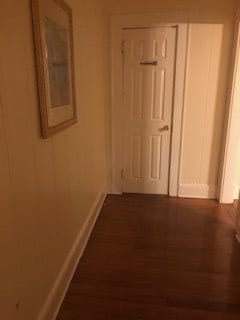 A quiet hallway with a wooden floor, white door, and framed picture hanging on the wall.