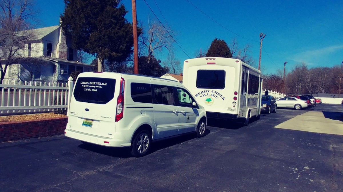A van and a bus parked in a parking lot on a sunny day.