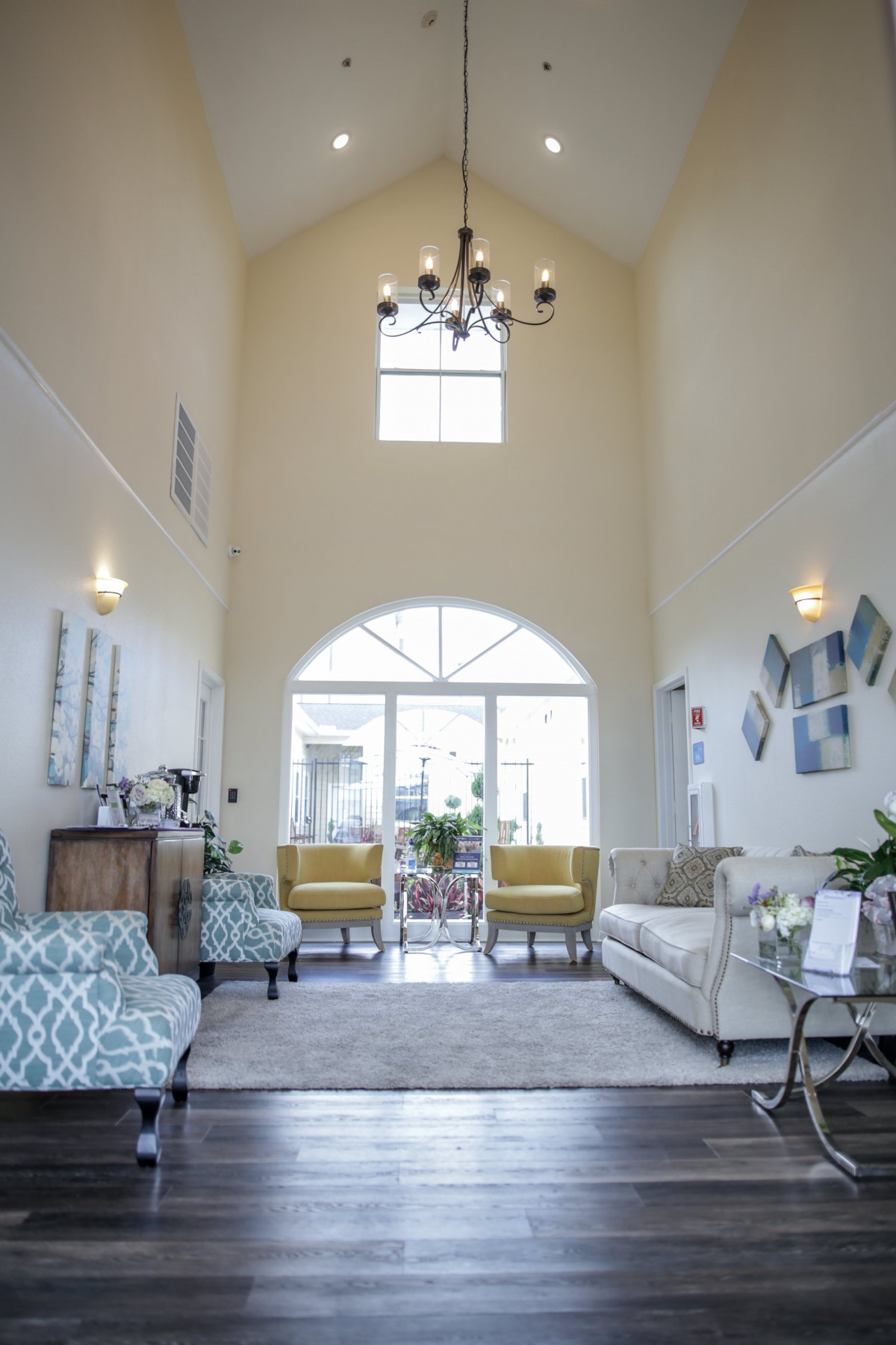 A spacious living room with high ceilings, featuring a chandelier, large windows, and stylish furniture.