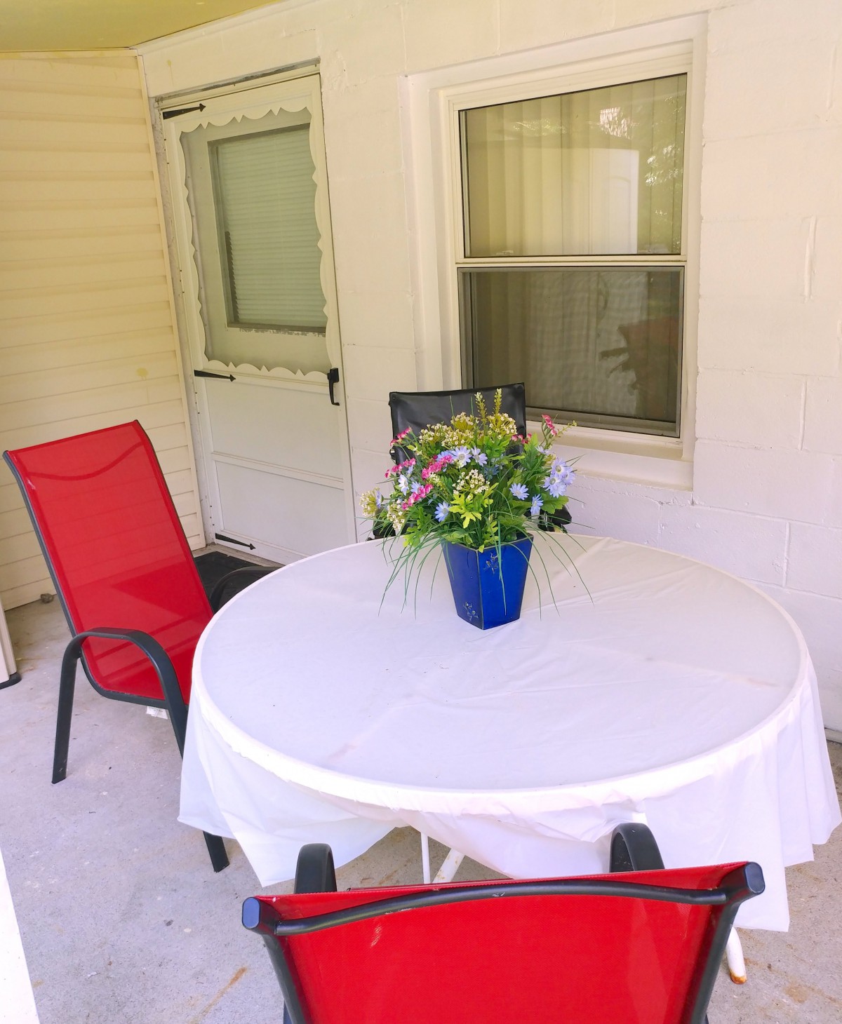 A cozy patio with a table set for relaxation, featuring red chairs and a floral centerpiece.