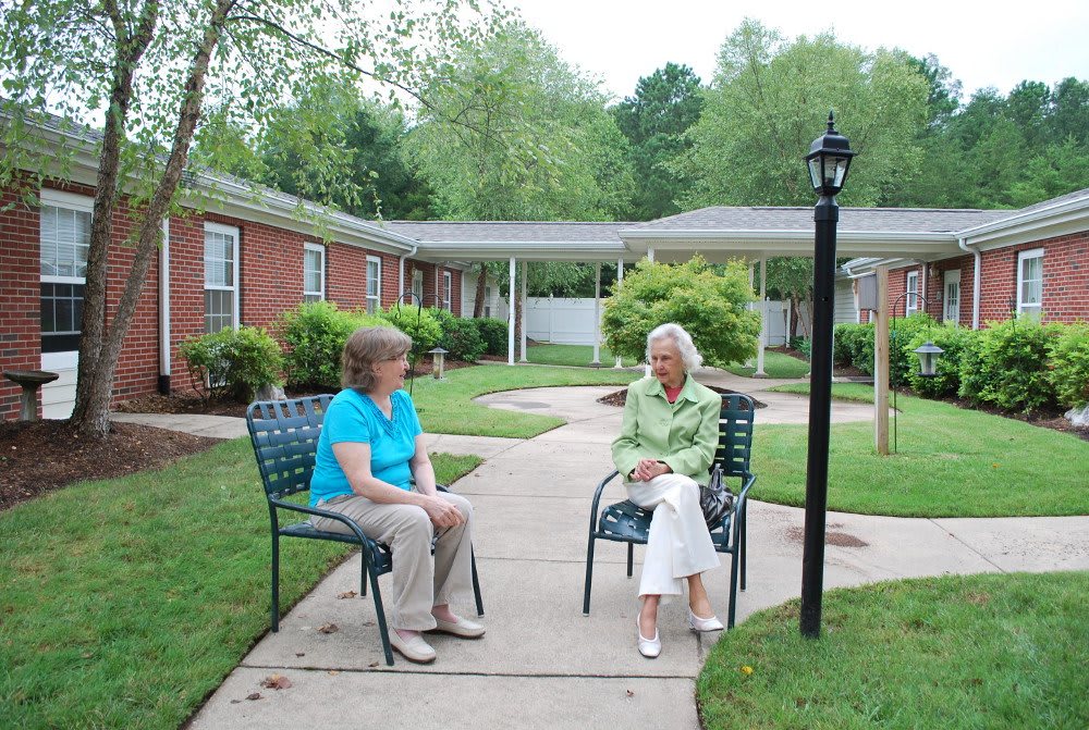 Two women sitting on chairs in a garden area engaged in conversation.