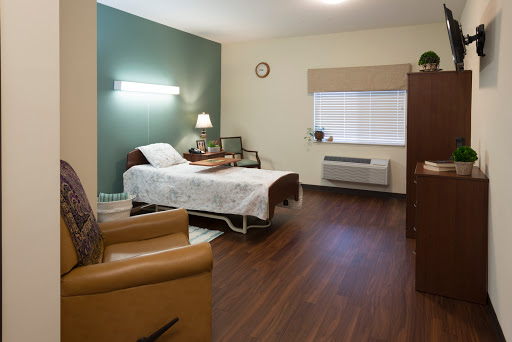 A well-furnished hospital patient room featuring a bed, chair, and natural light.