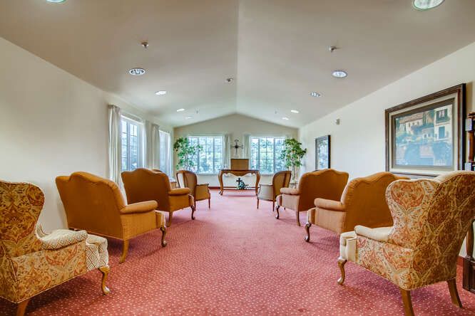 A spacious seating area with comfortable chairs and large windows, complemented by potted plants and a carpeted floor.