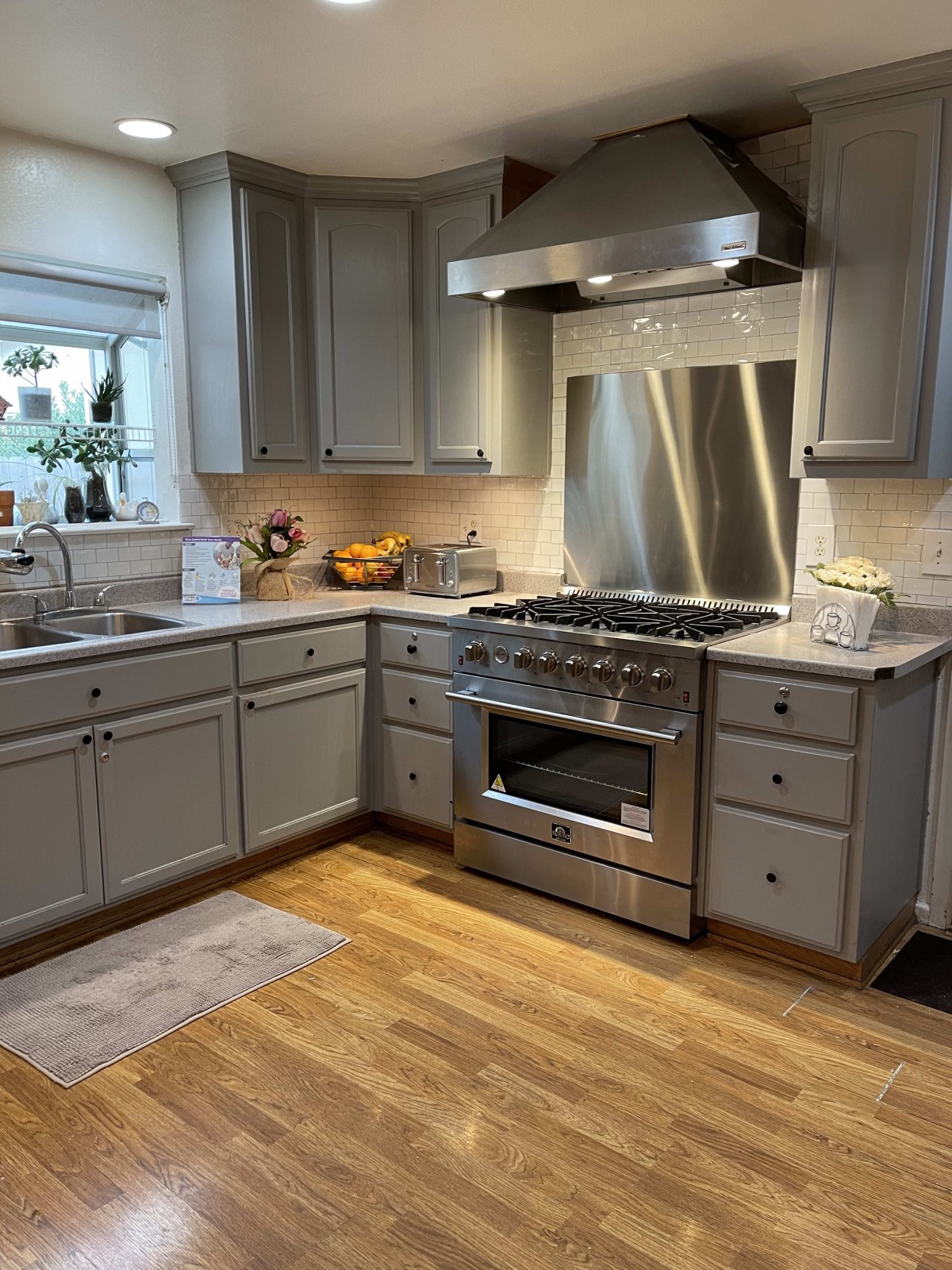 A modern kitchen with gray cabinets, a stainless steel stove, and hardwood floors.