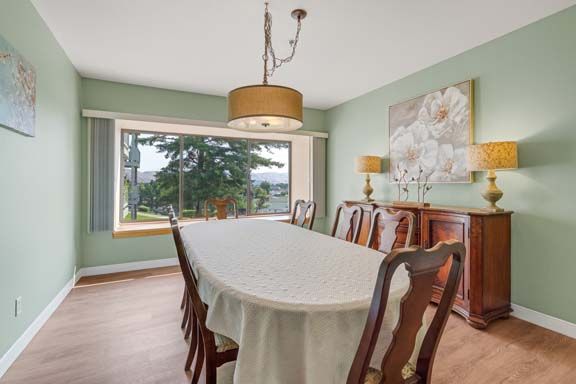 A well-appointed dining room with a long table and chairs, featuring a large window, chandelier, and decorative artwork.