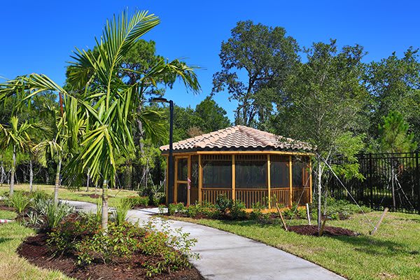 A scenic garden view featuring a gazebo with a tiled roof, surrounded by lush greenery and a winding pathway.