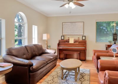 A cozy living room featuring a sofa, armchair, and piano, with a coffee table centered on a patterned rug.