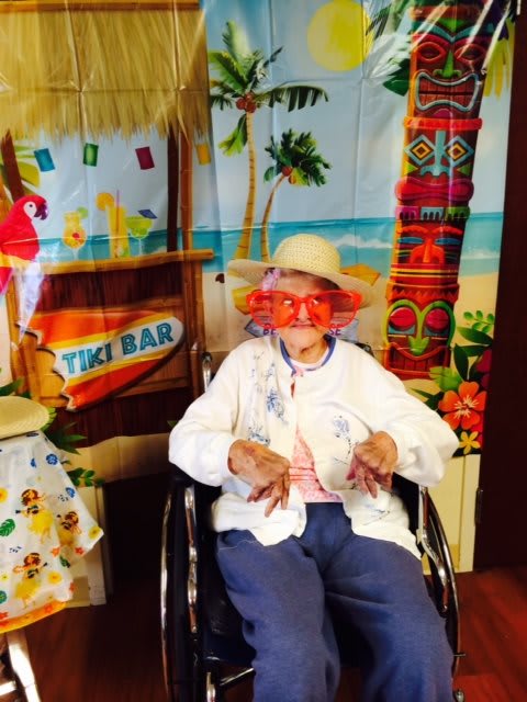 A person in a wheelchair is enjoying a tropical-themed event, wearing a hat and fun glasses.