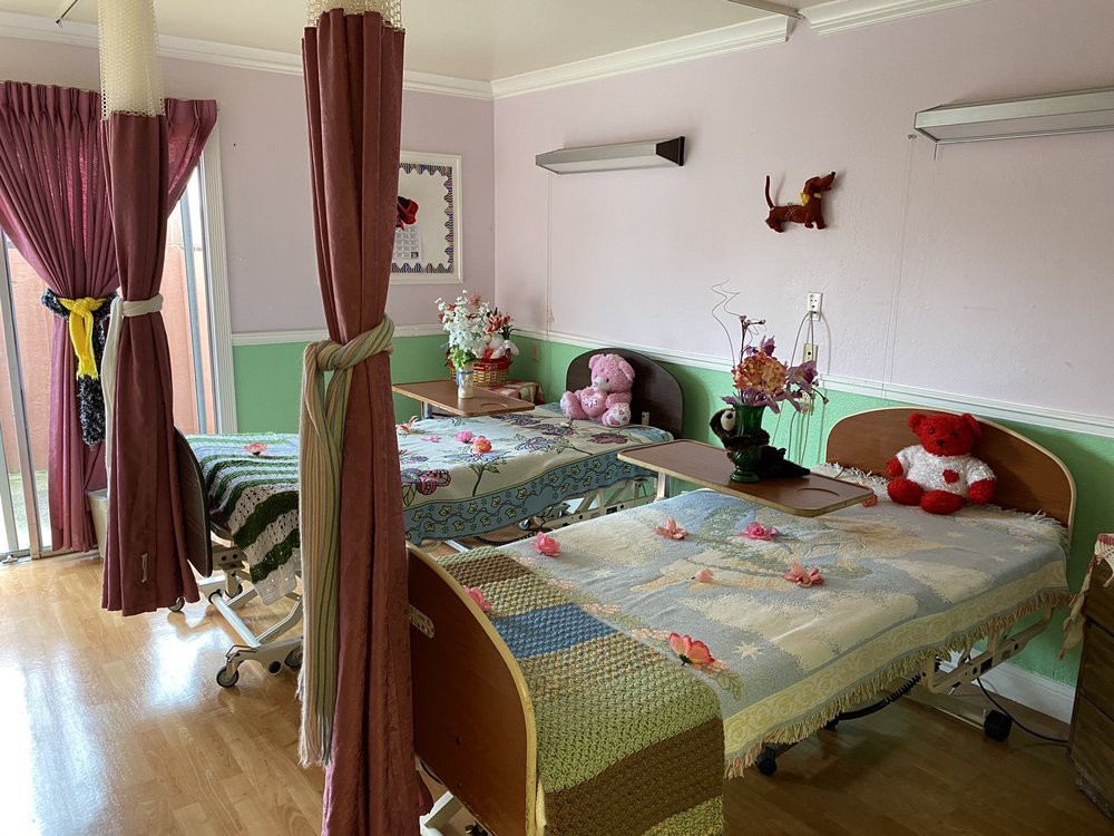 A hospital room with two beds, separated by curtains and decorated with flowers and plush toys.