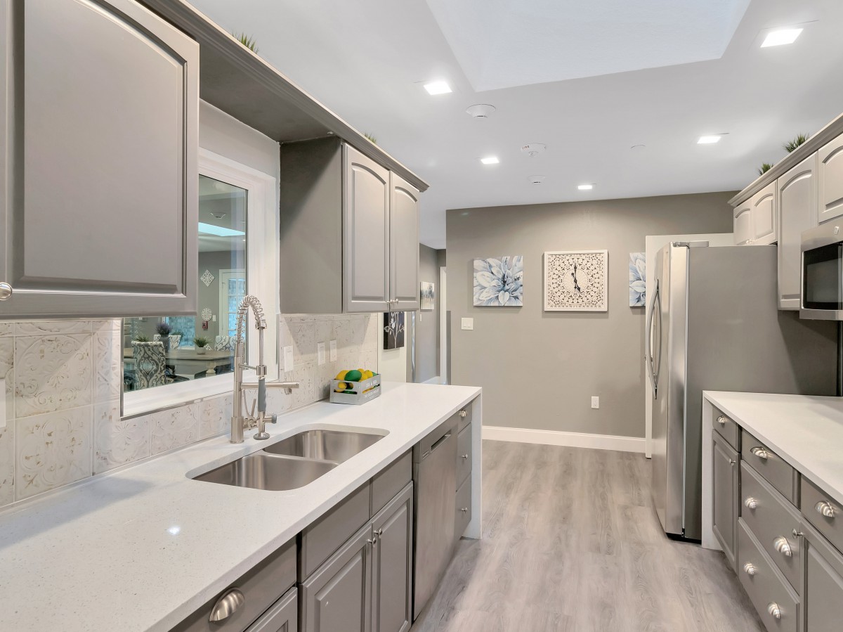 A modern kitchen with gray cabinets, white countertops, and stainless steel appliances.