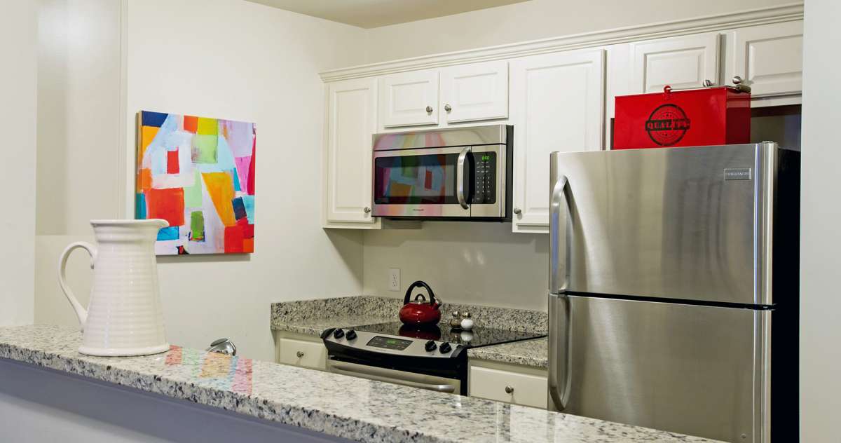 A modern kitchen with stainless steel appliances and granite countertops, featuring colorful artwork on the wall.