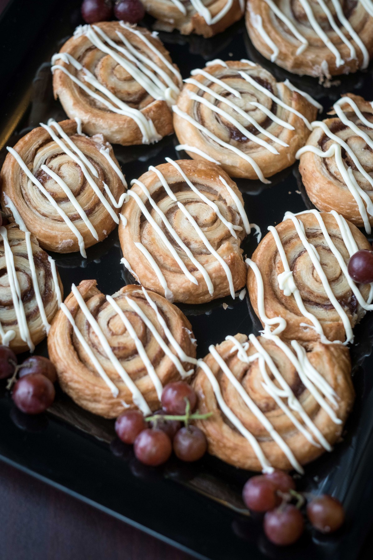 Freshly baked cinnamon rolls drizzled with icing, accompanied by grapes.