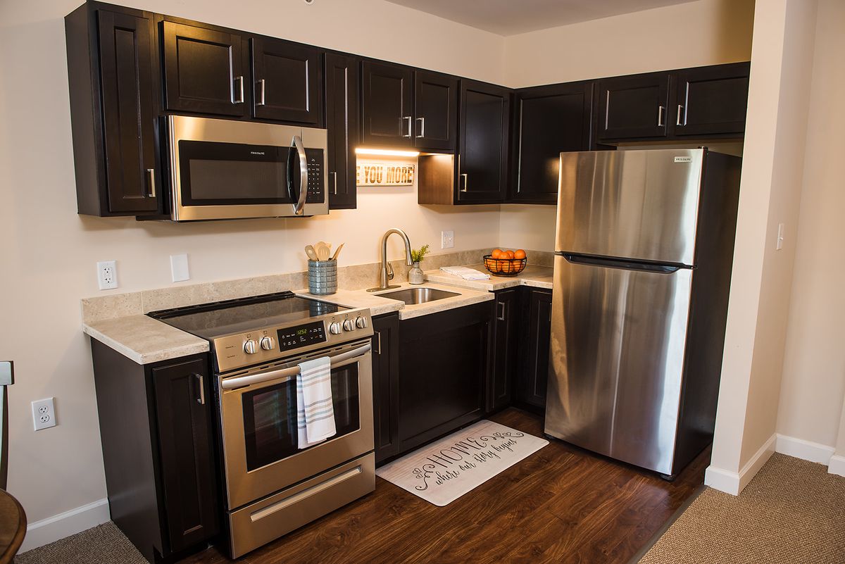 A modern kitchen with dark cabinets, stainless steel appliances, and hardwood flooring.