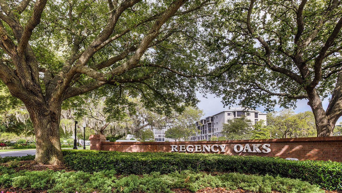 Entrance sign of the Regency Oaks apartment complex surrounded by lush trees and greenery.