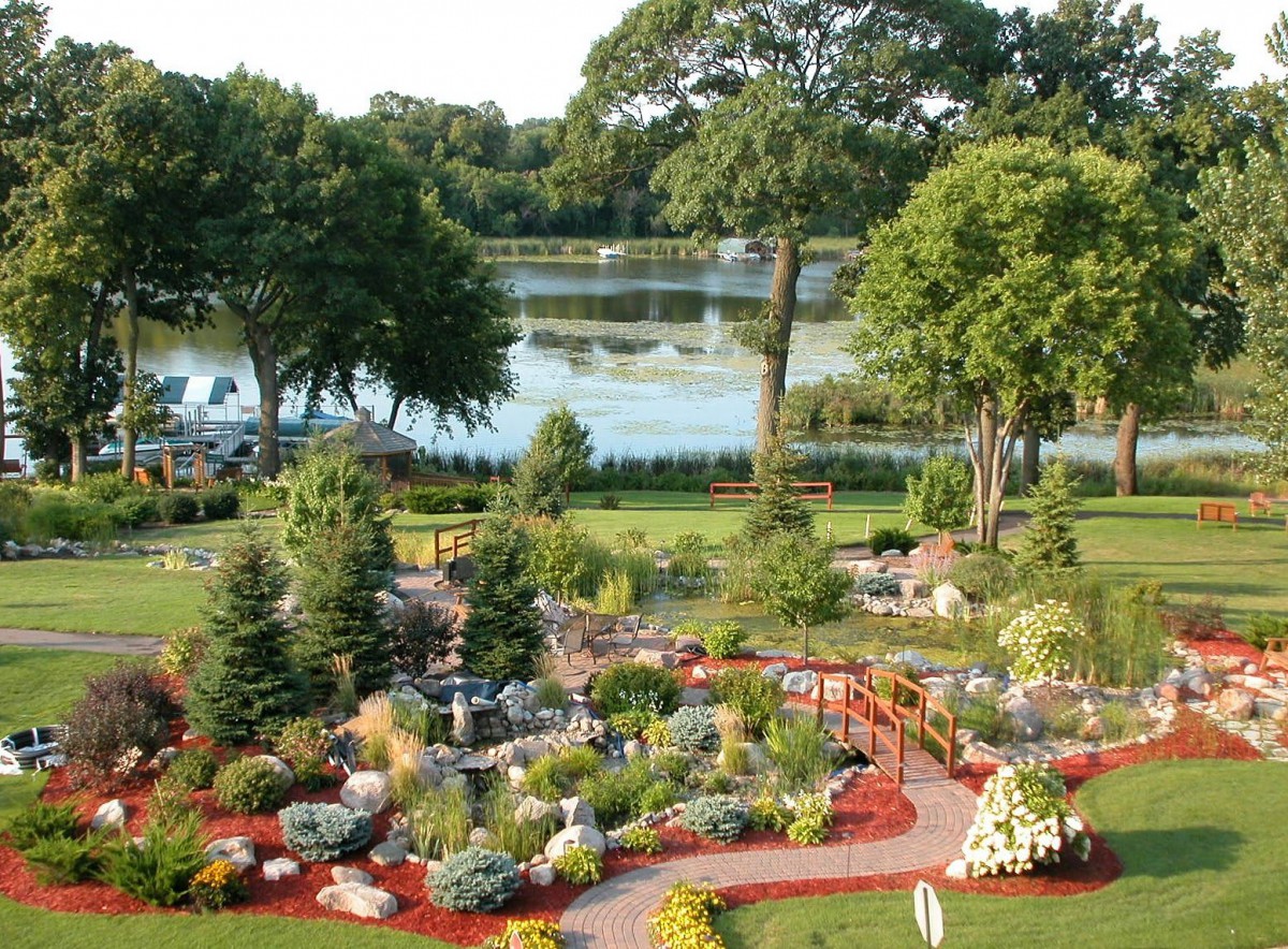 A beautifully landscaped garden with colorful flowers and trees, set beside a tranquil lake.