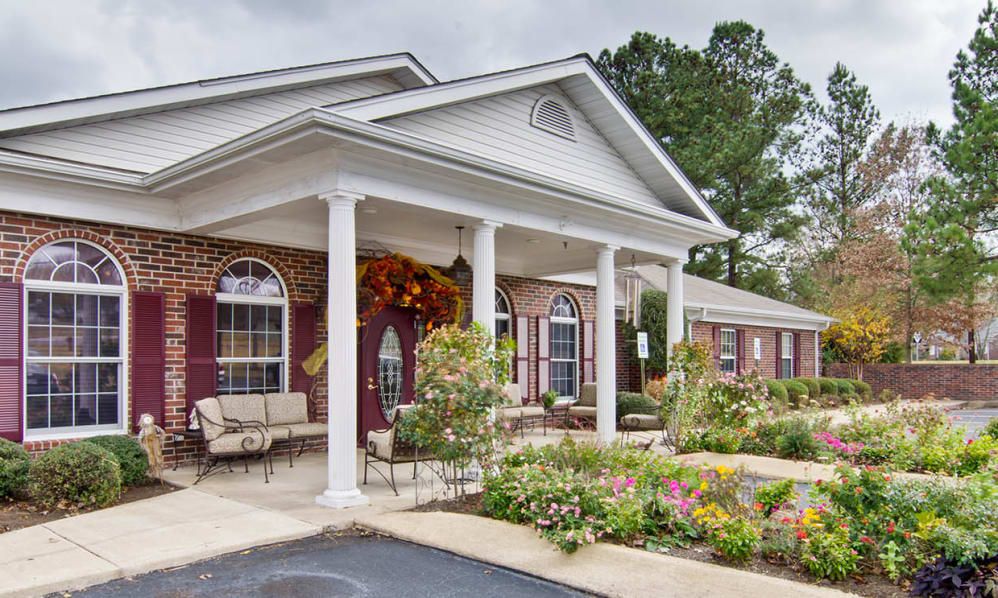 A well-maintained building with a garden in front and a welcoming porch supported by columns.