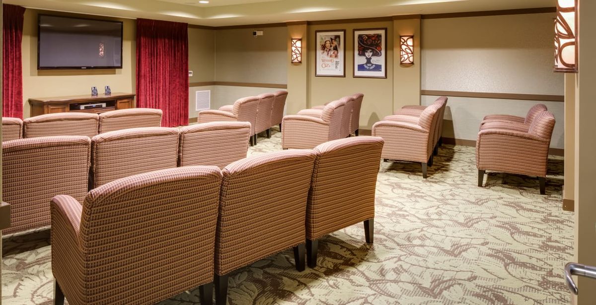 A cozy theater-style room with rows of upholstered chairs facing a screen, adorned with wall art and warm lighting.