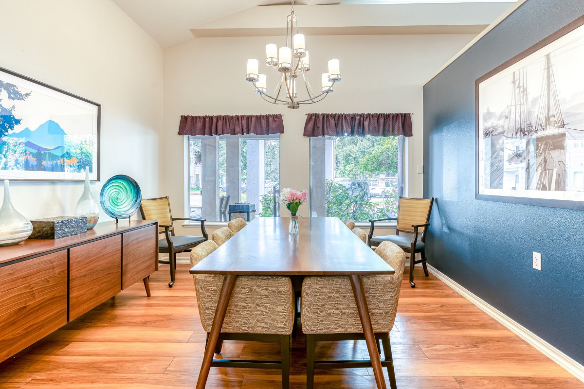 A bright and elegantly decorated dining room with a long wooden table, surrounded by chairs and lit by a chandelier.
