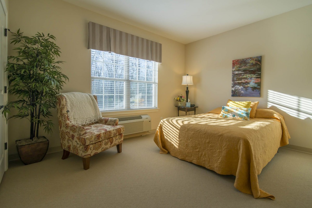 A cozy bedroom with a bed, chair, and a large window allowing natural light.