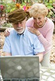 An elderly couple enjoying time together outdoors with a laptop.