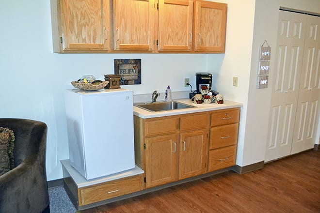 A compact kitchenette with a mini fridge, sink, and wooden cabinets.