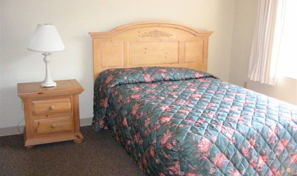 A bedroom with a wooden headboard, floral quilt, and a matching nightstand.