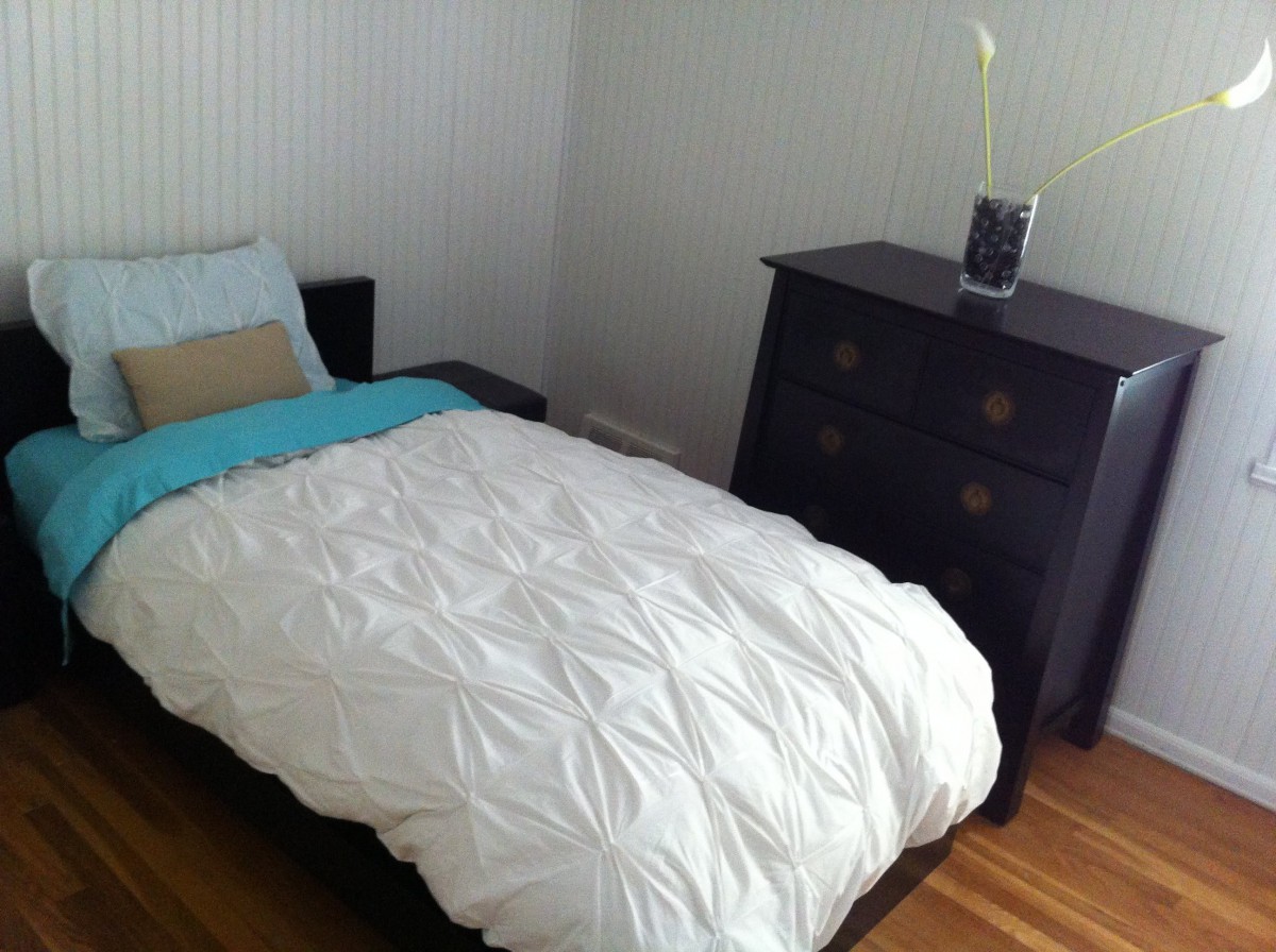 A minimalist bedroom with a single bed and a dark wooden dresser.