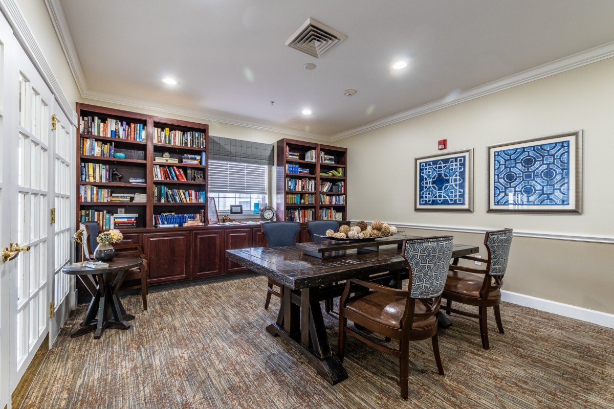 A cozy library room with wooden bookshelves and a large table surrounded by chairs, creating a perfect study or reading environment.