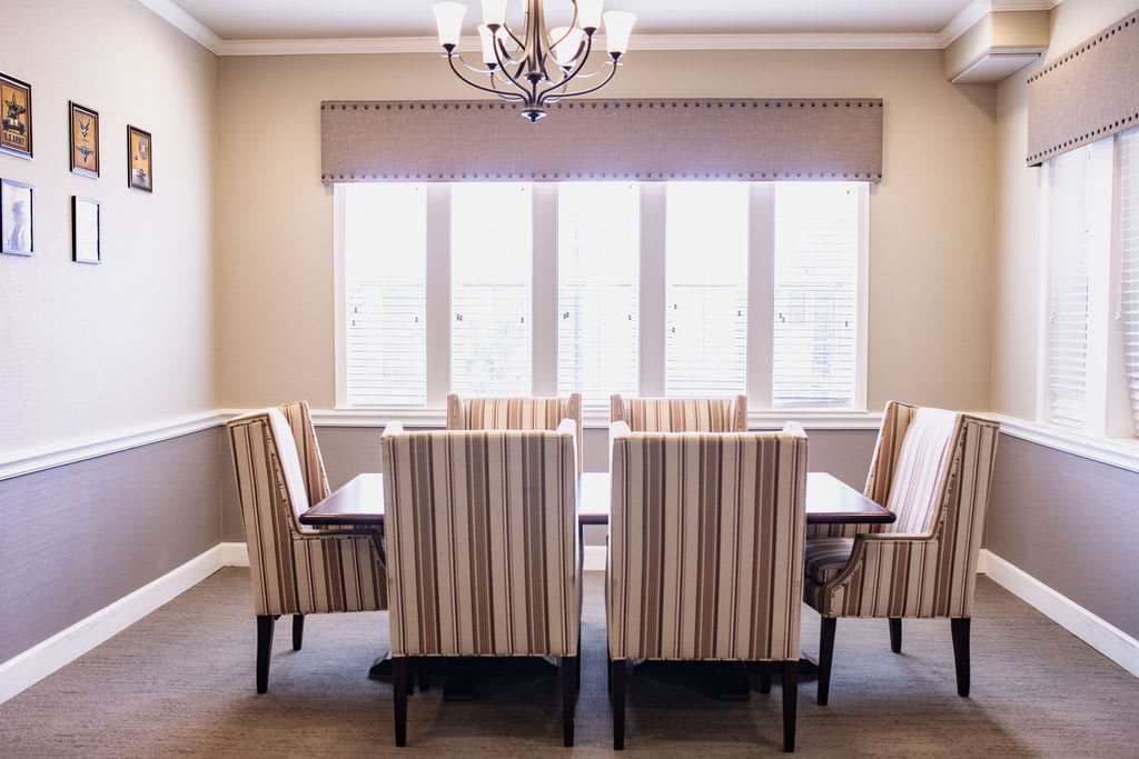A dining room with a set of six striped upholstered chairs around a wooden table, illuminated by a chandelier and natural light from the window.