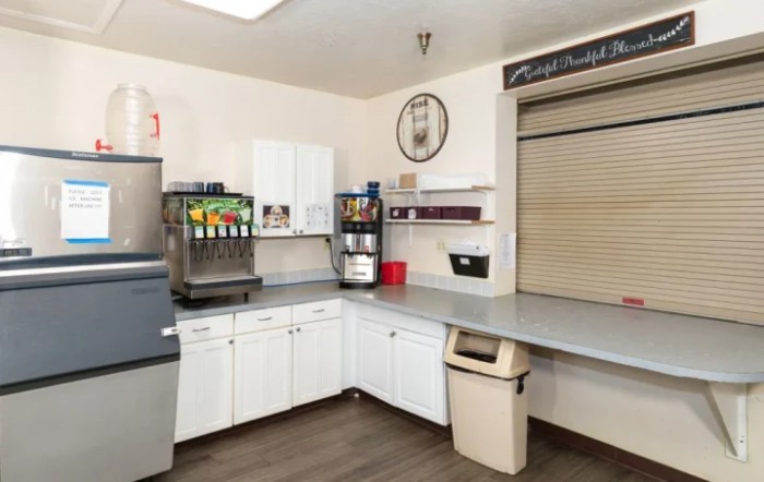 A clean cafeteria kitchen area with a soda dispenser, coffee machine, and storage cabinets.