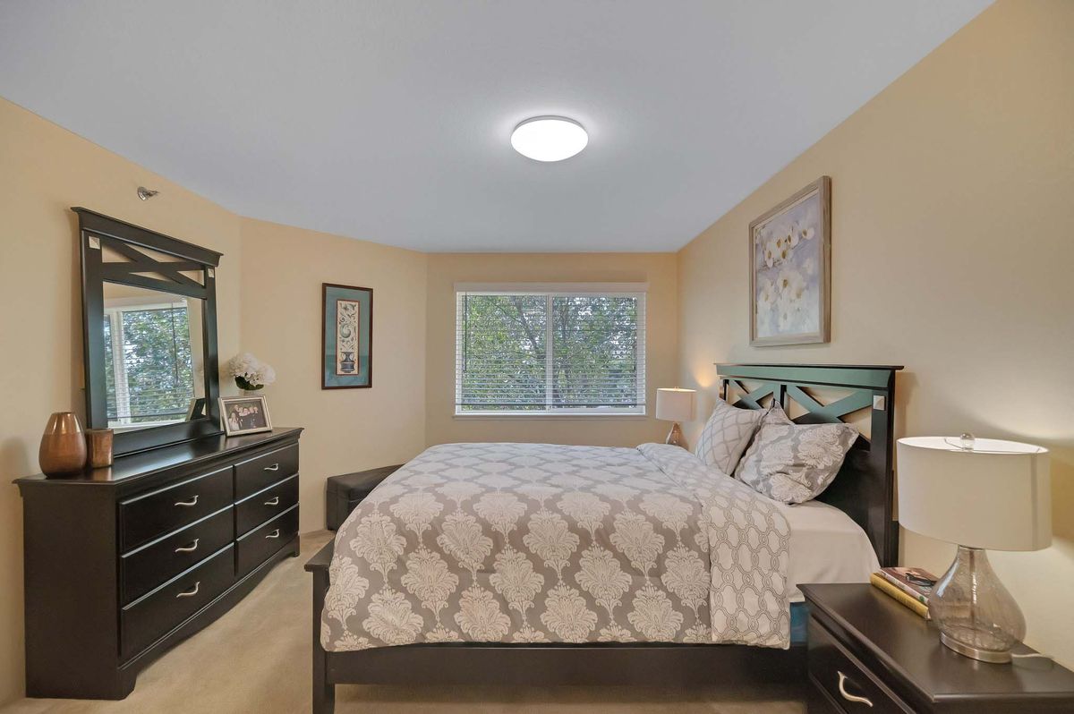 A cozy bedroom with a large bed, dresser, and window adorned with wall art.