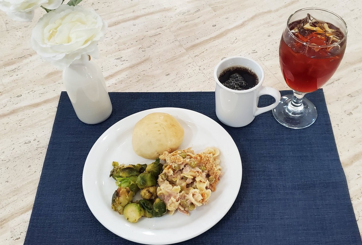 A dinner plate with broccoli, casserole, and a roll, accompanied by coffee and juice.