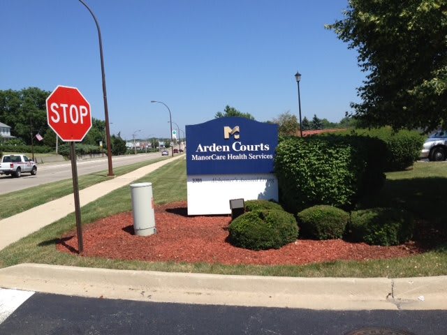 A healthcare facility sign near a stop sign, surrounded by well-maintained landscaping.