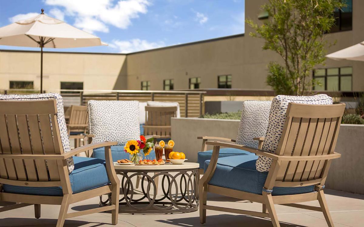 A cozy outdoor patio setup with chairs and a table adorned with sunflowers and drinks under a clear sky.