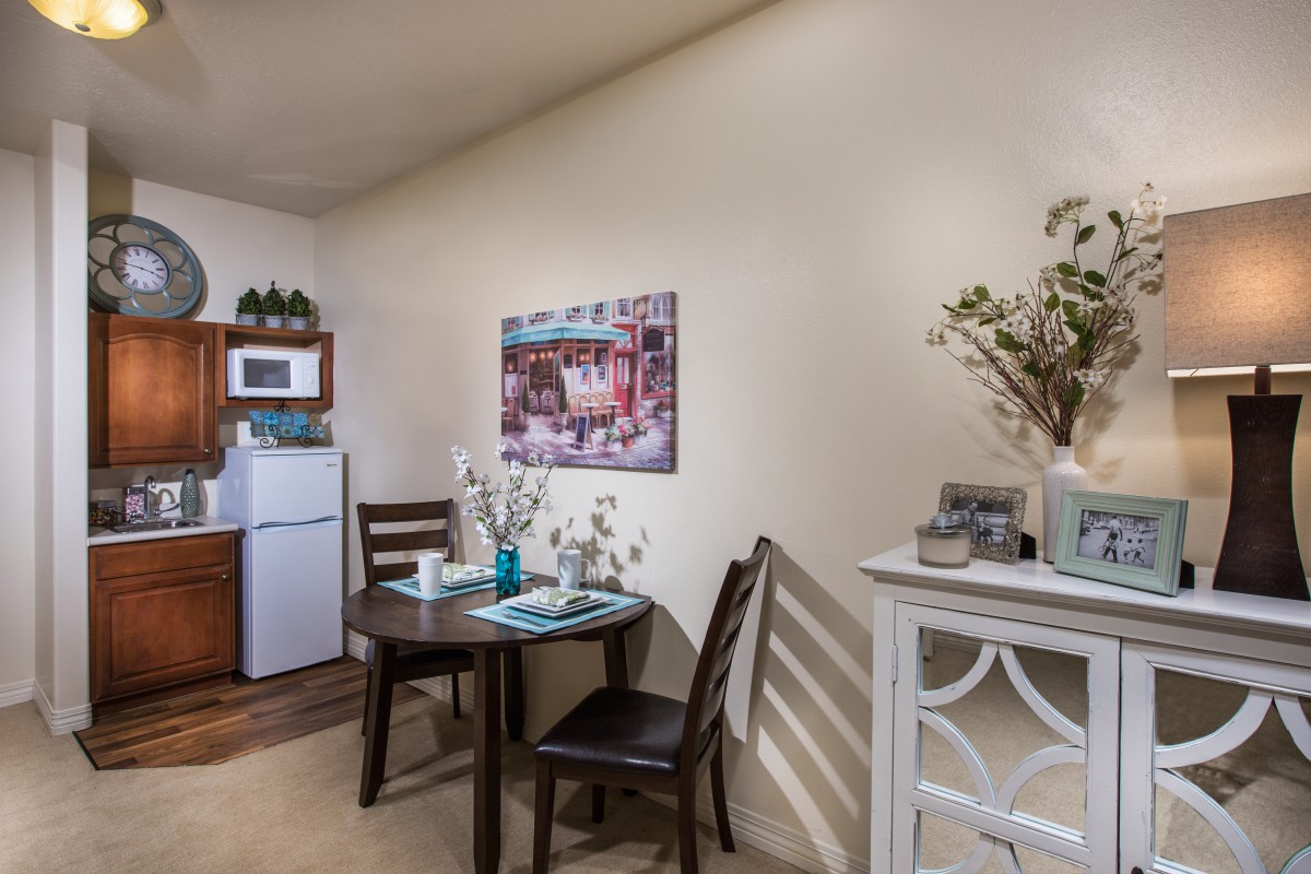 A cozy kitchen and dining area featuring a small table with chairs, a refrigerator, microwave, and decorative elements.
