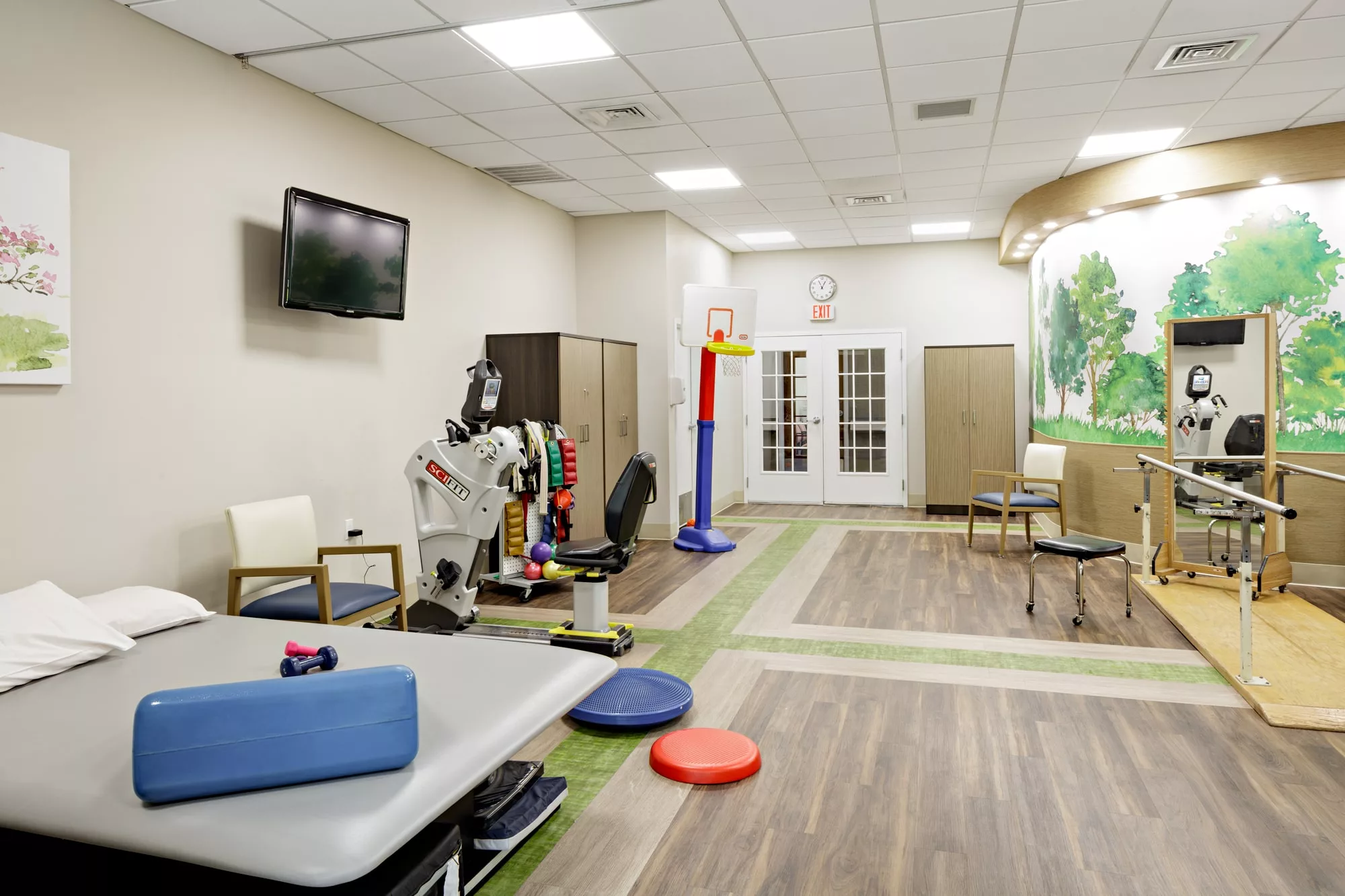 A bright rehabilitation room equipped with various physical therapy tools and exercise mats.