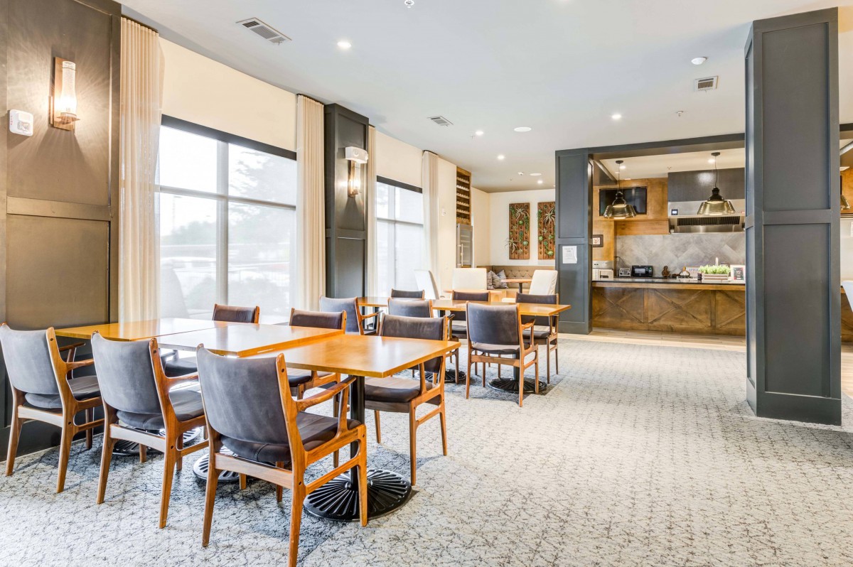 A modern dining area with wooden tables and chairs, featuring large windows and comfortable seating.