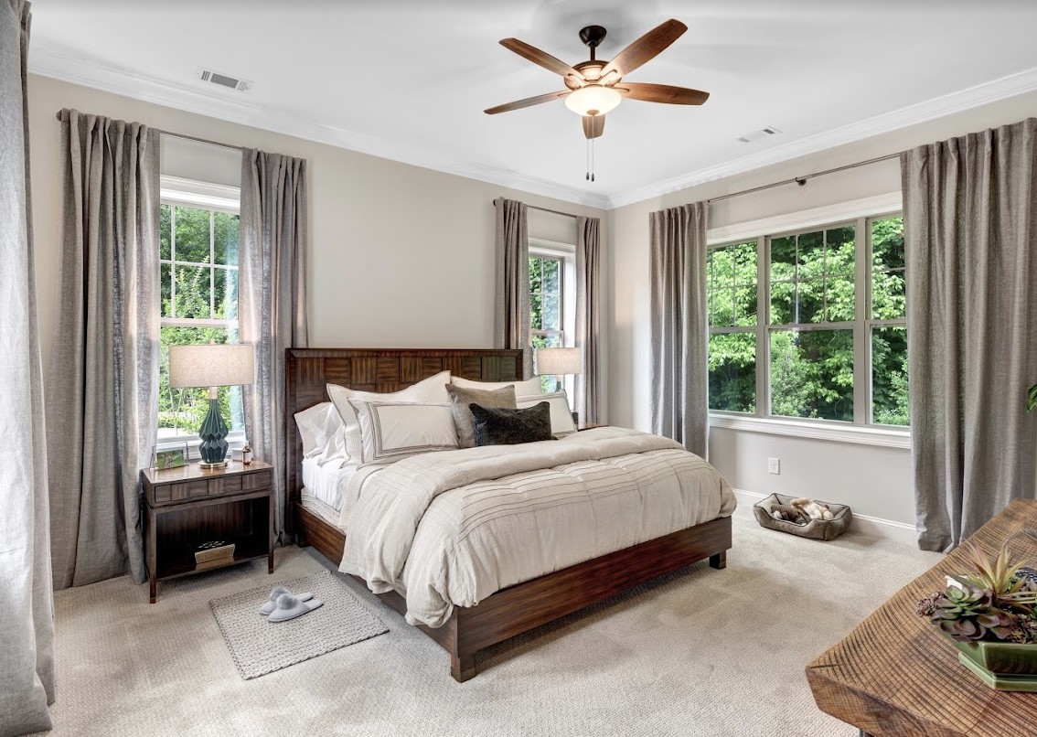 A cozy bedroom with a large bed, surrounded by windows and elegant curtains.