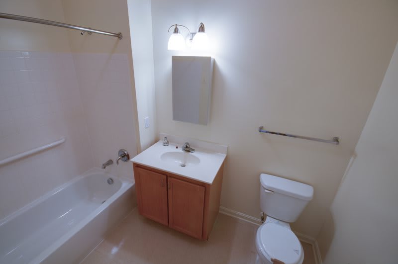 A clean and simple bathroom with a bathtub, sink, cabinet, toilet, and mirror.