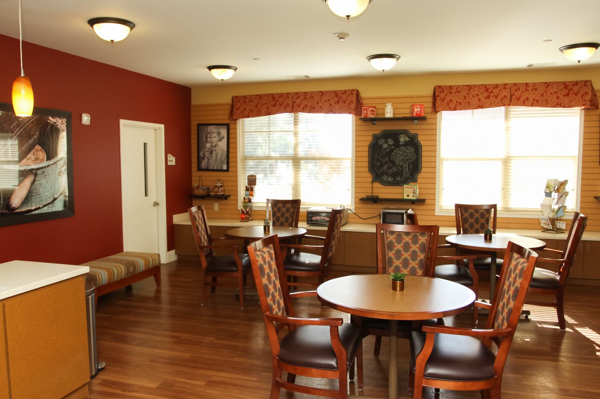 A cozy dining area with round tables and chairs, featuring warm decor and large windows.